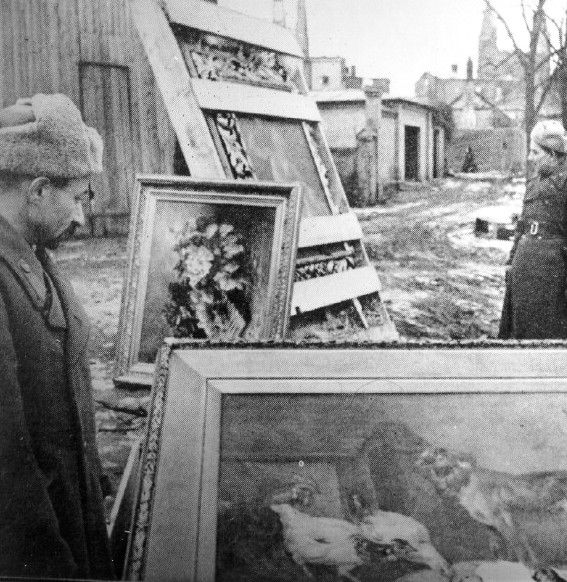 Red Army soldiers standing beside paintings and art objects looted from the USSR and later found in East Prussia.